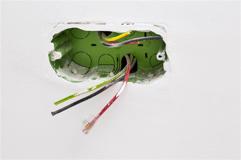Loose electrical wires protruding from a green wall-mounted back box.