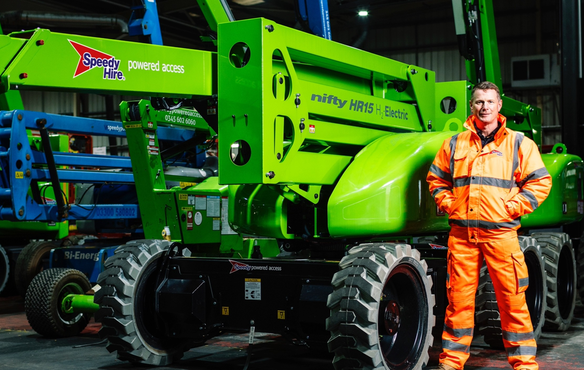 Green electric-powered access platform with Speedy Hire branding inside an industrial facility with a Speedy Hire staff