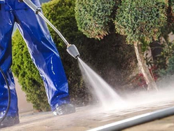 a worker in blue using a pressure washer to clean the ground
