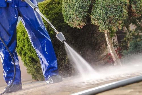 a worker in blue using a pressure washer to clean the ground