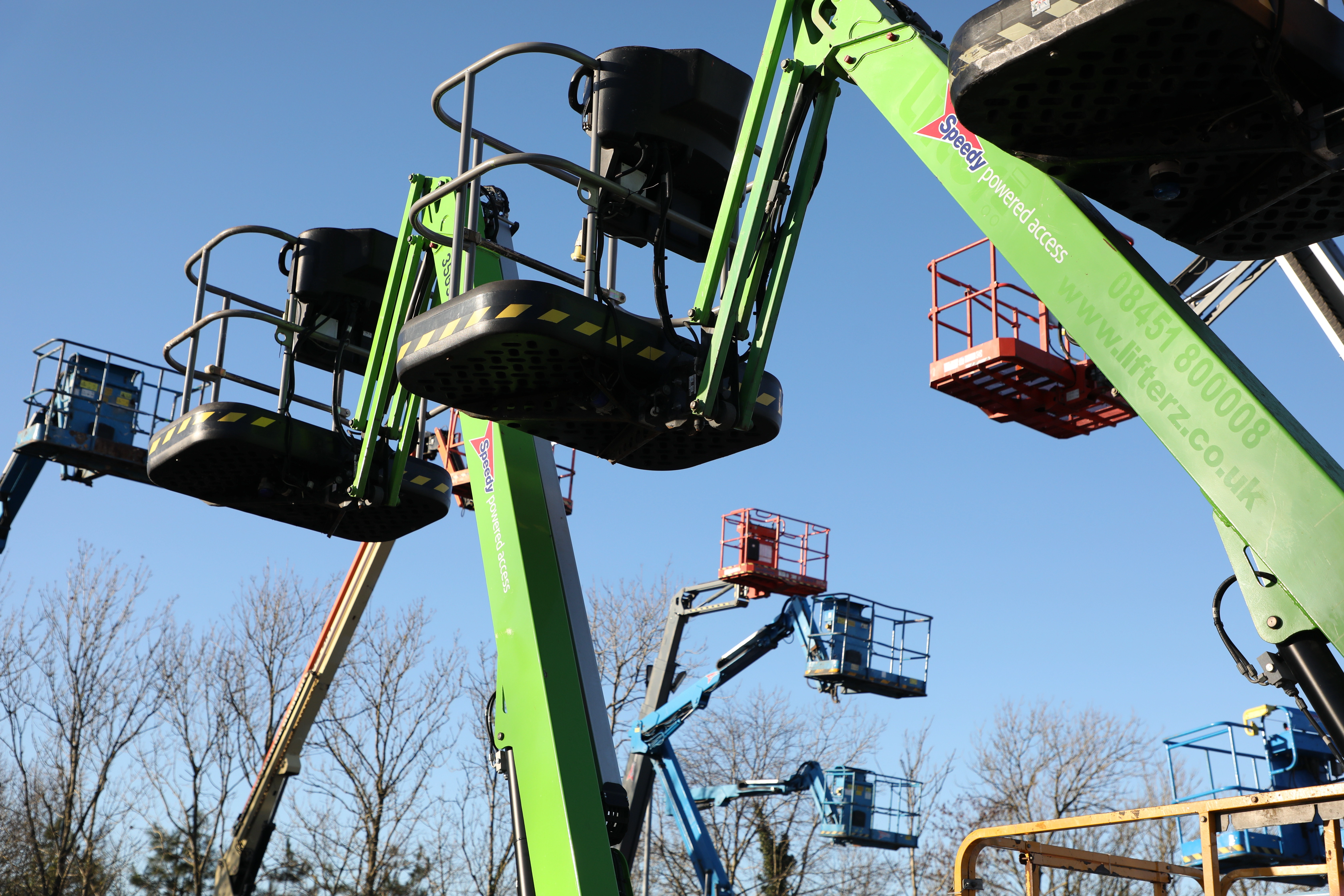 Speedy Hire powered access lifts on a construction site under clear blue skies.