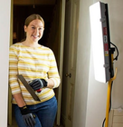 Woman standing in a doorway holding a trowel, illuminated by a bright work light during a DIY project.