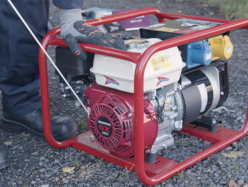 A person wearing protective gloves pulls the start cord on a portable petrol generator with a red frame and Honda GX engine.