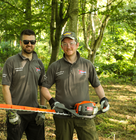 Two Speedy staff members holding a hedge trimmer while standing in a wooded area.