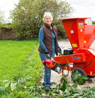 Person standing outdoors beside a red Speedy wood chipper, preparing to shred garden branches on a grassy area.