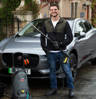 Person standing in front of a car holding a pressure washer during car cleaning.
