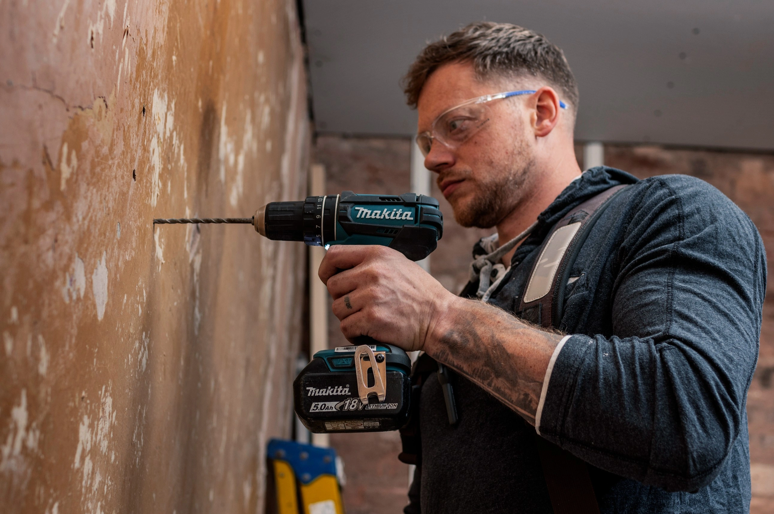  a man using makita hammer drill to drill the wall