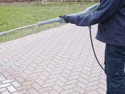 Person using a pressure washer to clean a brick patio.