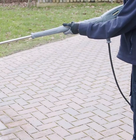 Person using a pressure washer to clean a brick patio.