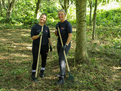Two smiling people wearing work gloves and holding rakes in an autumn garden