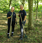 Two smiling people wearing work gloves and holding rakes in an autumn garden