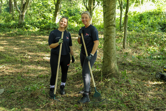Two smiling people wearing work gloves and holding rakes in an autumn garden