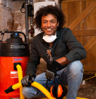 Person wearing gloves and a dust mask kneeling next to a large red Numatic vacuum unit