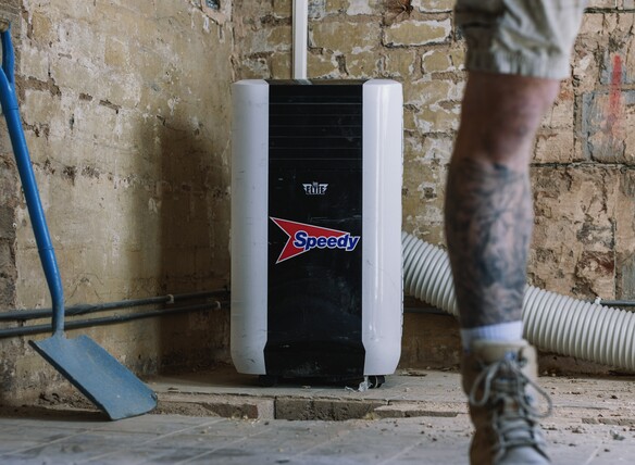 Portable air conditioner unit in a renovation space with exposed brick walls and tools nearby.