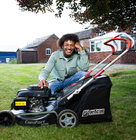 A smiling person sitting on grass beside a black Efco lawnmower