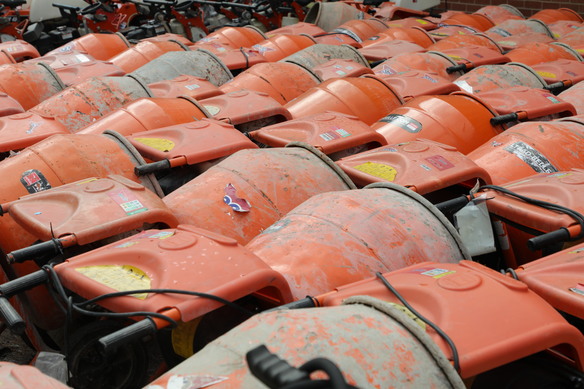 Rows of orange cement mixers arranged closely together, showing signs of wear and dried concrete splashes on their surfaces.