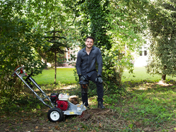 Person using a stump grinder to remove tree roots in a garden area.