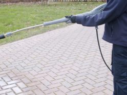 Person cleaning a brick driveway with a pressure washer