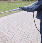 Person cleaning a brick driveway with a pressure washer