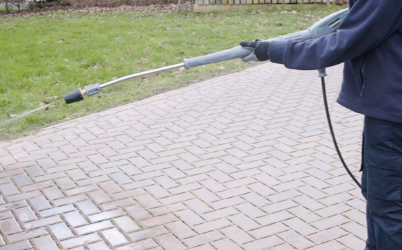Person cleaning a brick driveway with a pressure washer