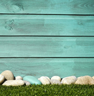 Smooth pebbles lined up on green grass in front of a turquoise wooden wall.