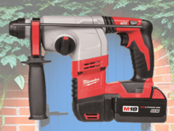 Red and gray Milwaukee cordless rotary hammer drill with black handle and battery pack, displayed against a background of a brick wall and blue wooden door with green foliage.