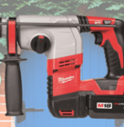 Red and gray Milwaukee cordless rotary hammer drill with black handle and battery pack, displayed against a background of a brick wall and blue wooden door with green foliage.