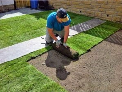 Person laying rolls of artificial grass on soil to create a new lawn in a garden.