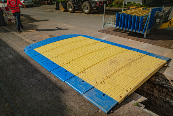 Heavy-duty yellow and blue road plate covering an open trench on a street