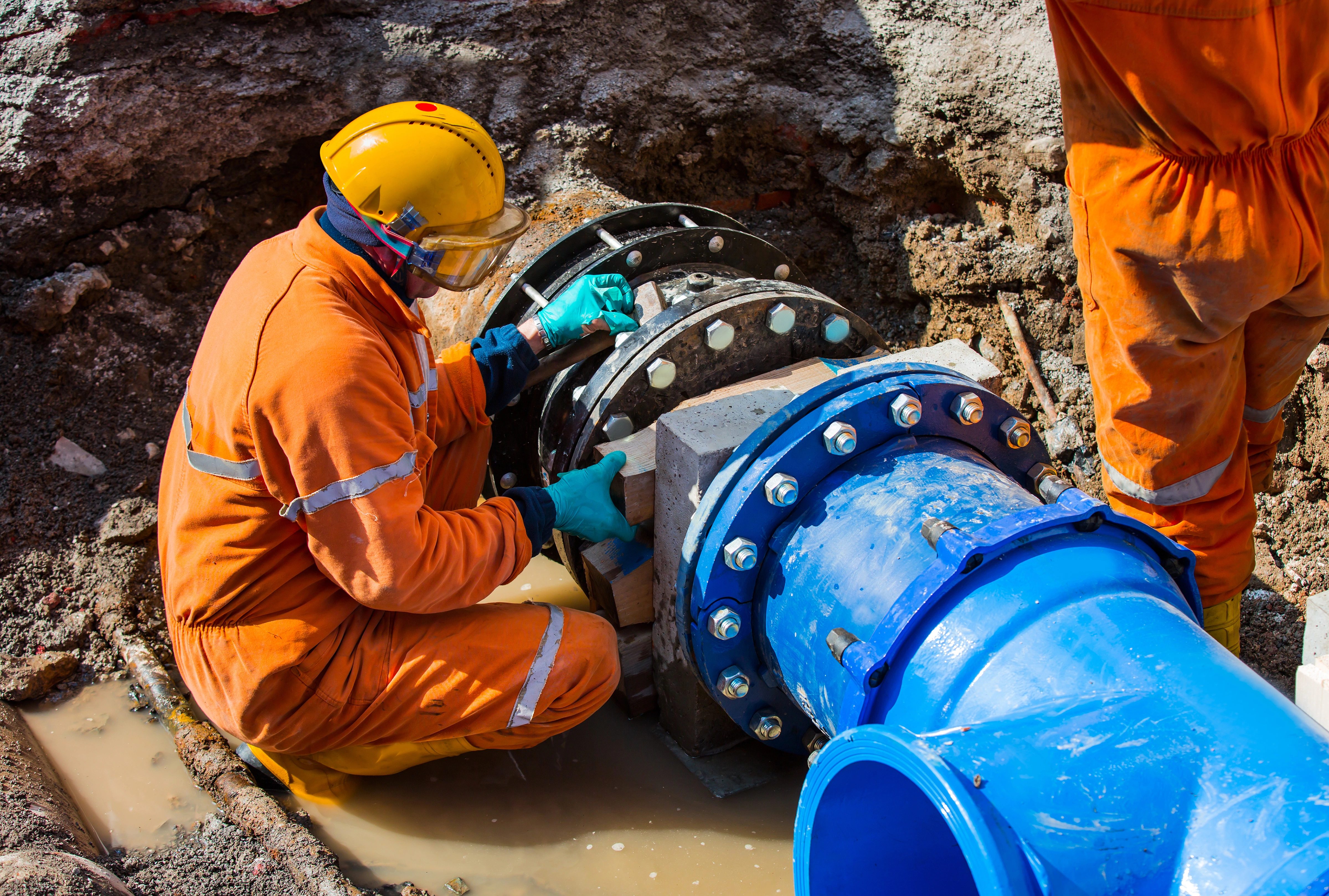 Construction worker in safety gear installing large underground water pipeline on a construction site.