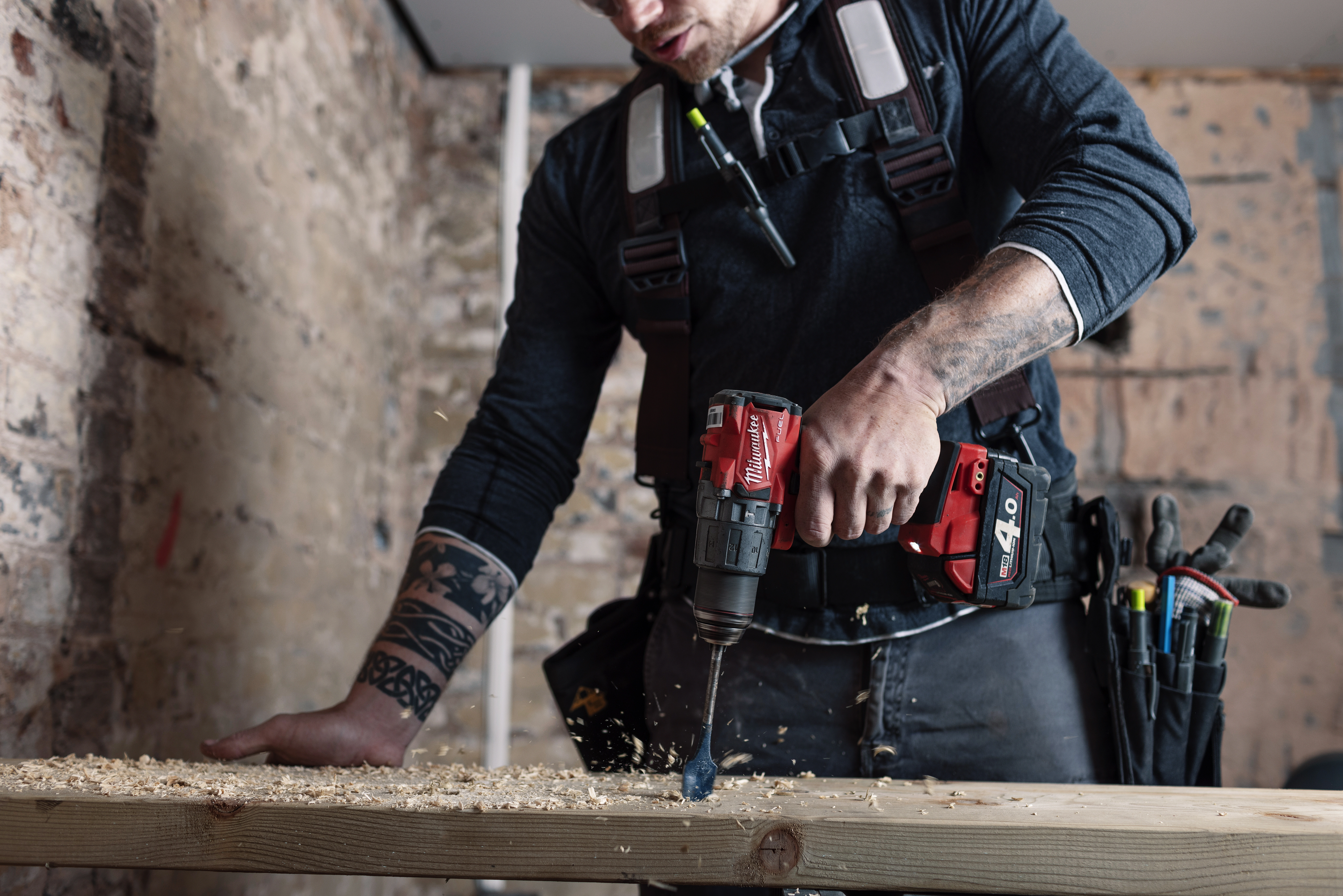a person using a Milwaukee cordless hammer drill to drill into a wooden plank on a DIY project