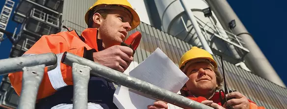 Construction workers wearing safety helmets and high-visibility jackets communicating on-site.