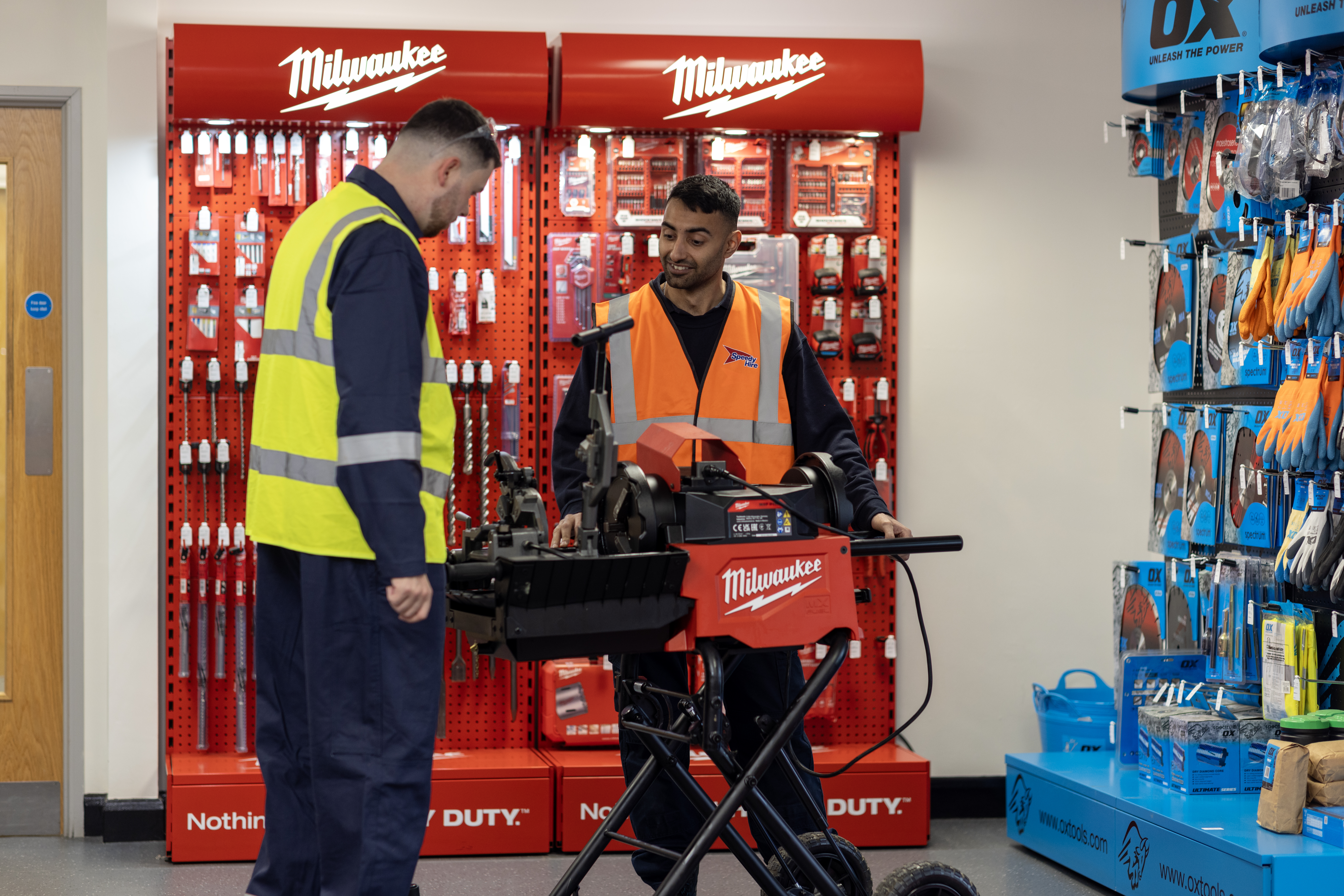 Speedy staff members demonstrate how to use a Milwaukee power tool inside a store