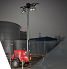 Red portable lighting tower with extended mast and LED floodlights, positioned outdoors near industrial tanks and fencing.