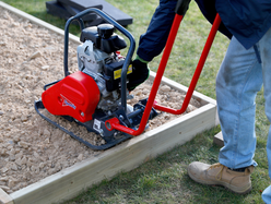 Person using a compactor plate to level and compact a sub base layer.