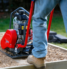 Person using a red plate compactor to level and compact soil on a construction site.