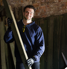 a person holding a long wooden plank in a workshop with a bright work light