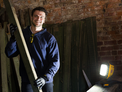 a person holding a long wooden plank in a workshop with a bright work light