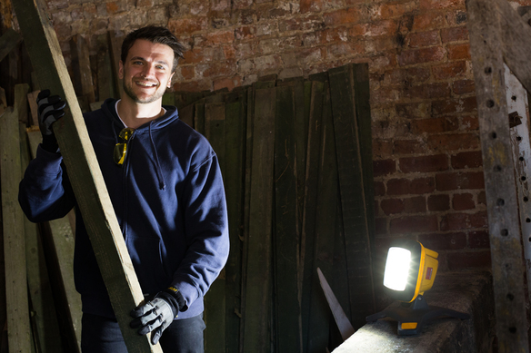 a person holding a long wooden plank in a workshop with a bright work light