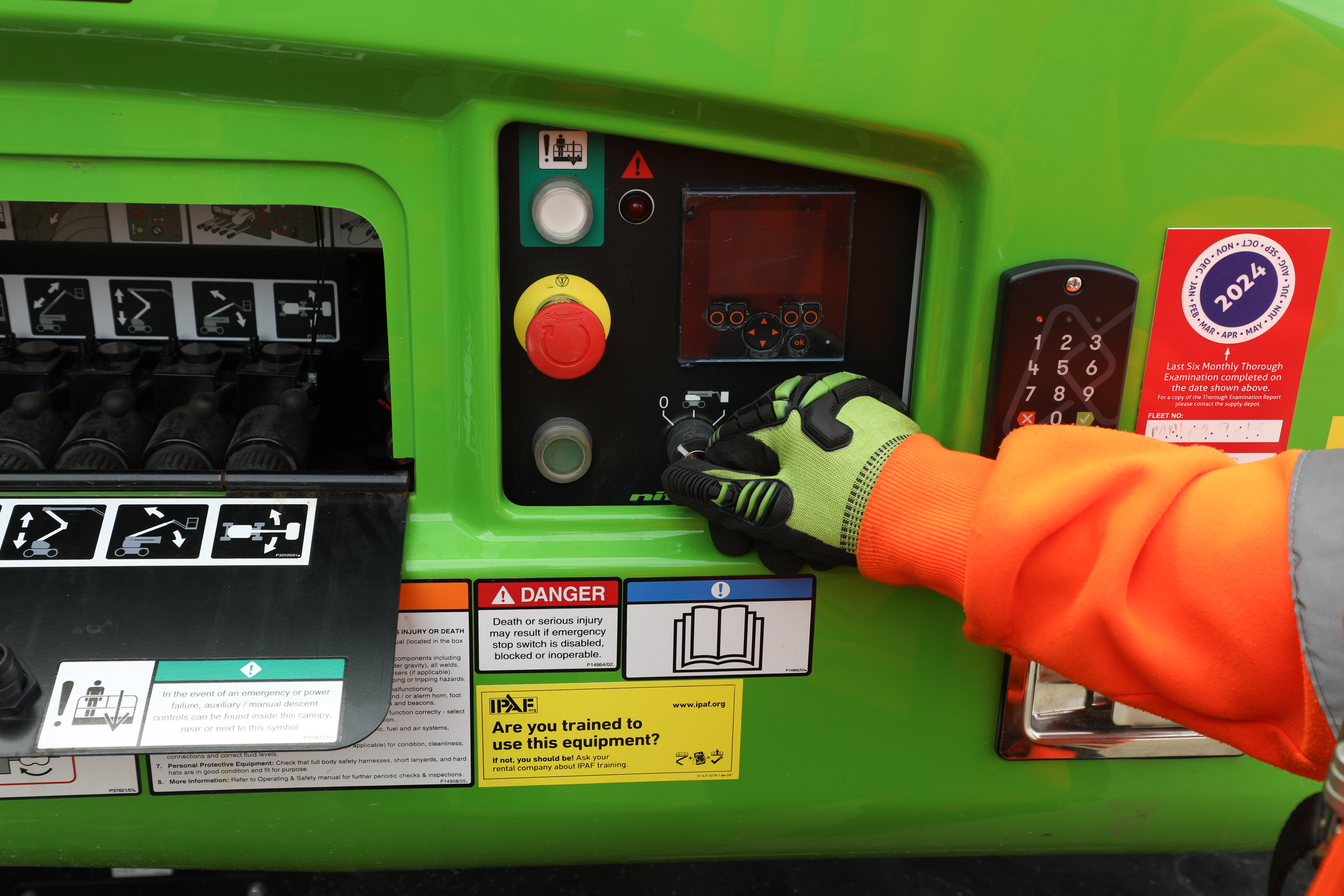 a worker operating a cherry picker control panel with a gloved hand.