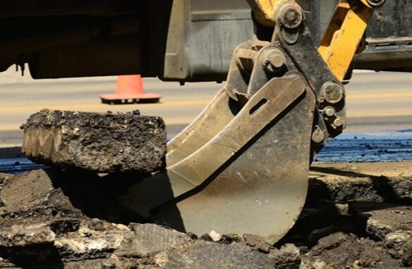 Excavator breaking asphalt during construction work on a road site.