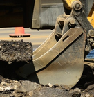 Excavator breaking asphalt during construction work on a road site.