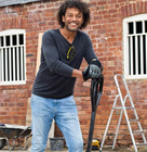 a person using a long-handled tool to work on the ground in front of a red brick building