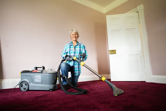 A person uses a professional carpet extraction cleaner on a deep red carpet in an empty room, operating the hose and floor wand attachment.