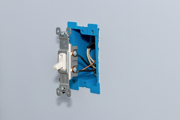 Partially installed light switch fitted into a blue electrical wall box.