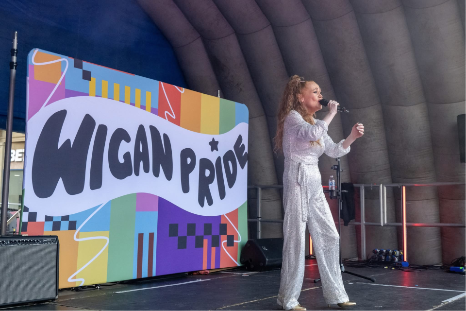 a performance on stage with wigan pride banner behind
