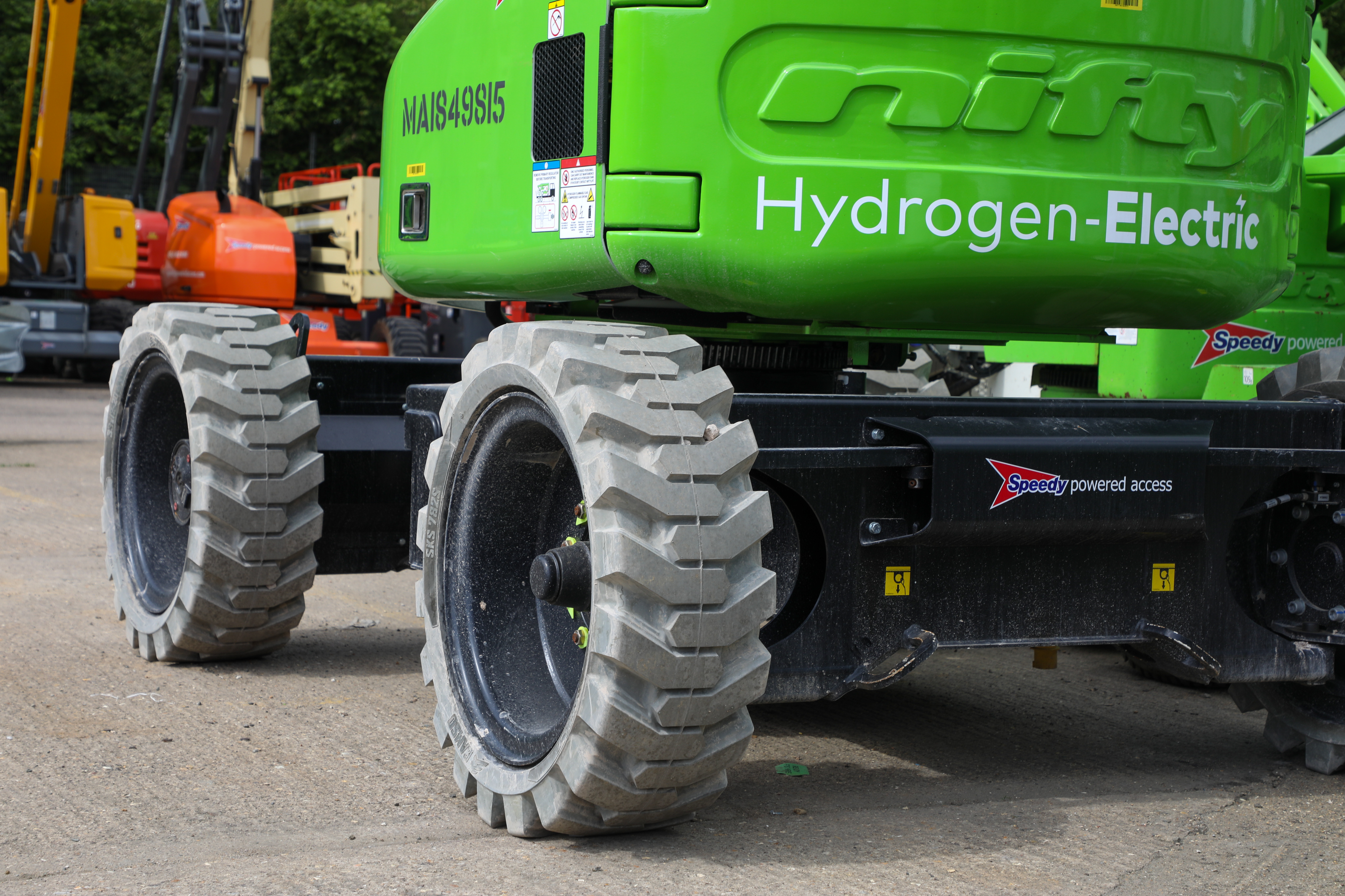 Close-up of a green self-propelled hydrogen‑electric cherry picker showing its large off‑road tyres.