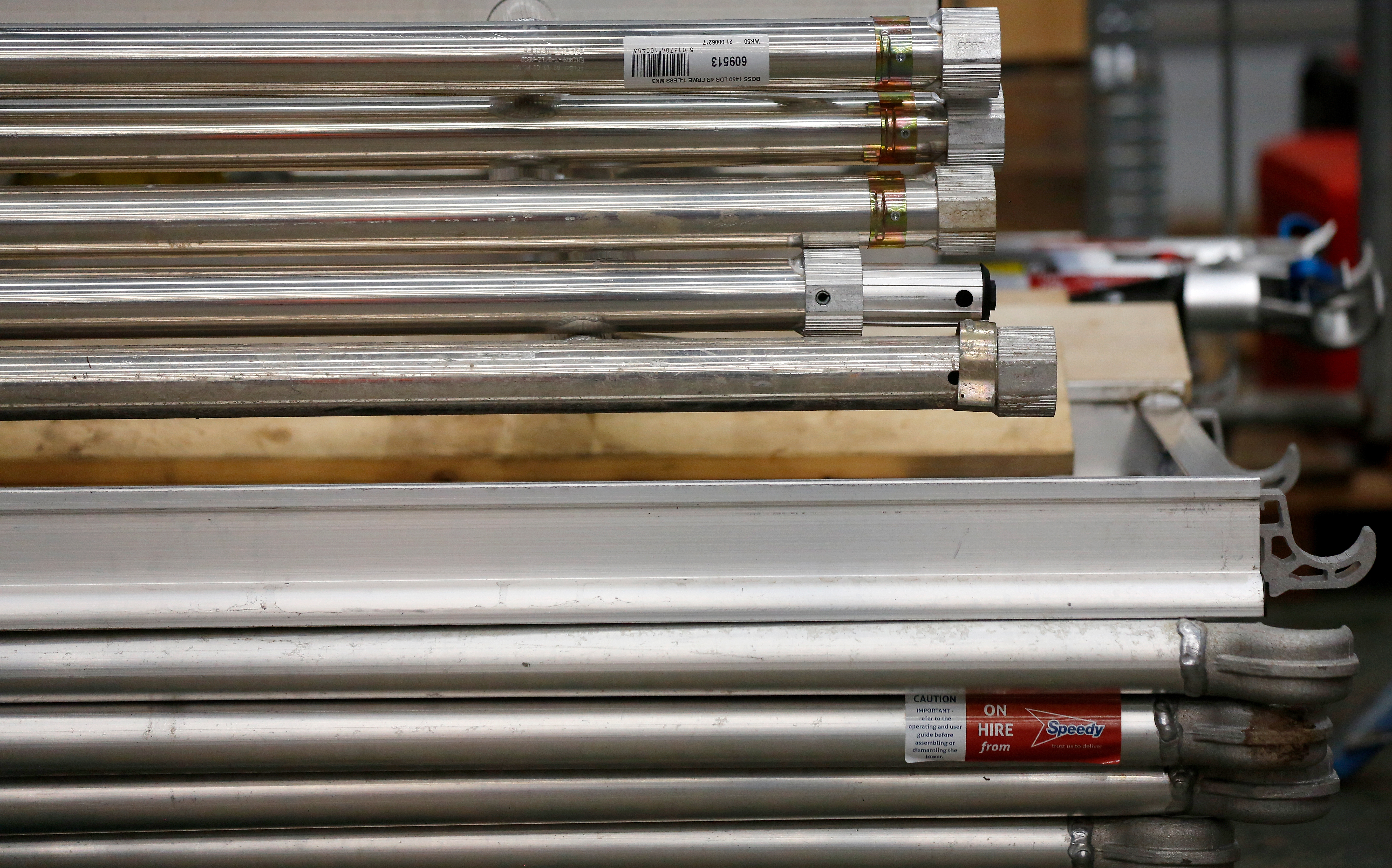 Close-up of stacked aluminum scaffold components, including horizontal braces and platform frames, with visible Speedy Hire labels and barcodes