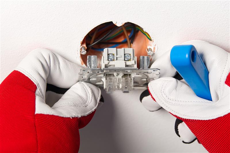 An electrician wearing protective gloves is installing a wall socket with exposed wiring.